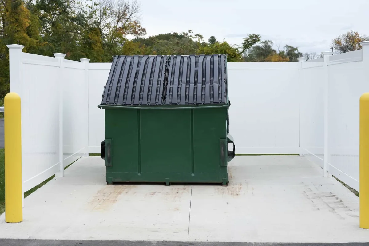 Finished dumpster pad with yellow bollards inside a vinyl enclosure in Western NC - The Western NC Concrete Company